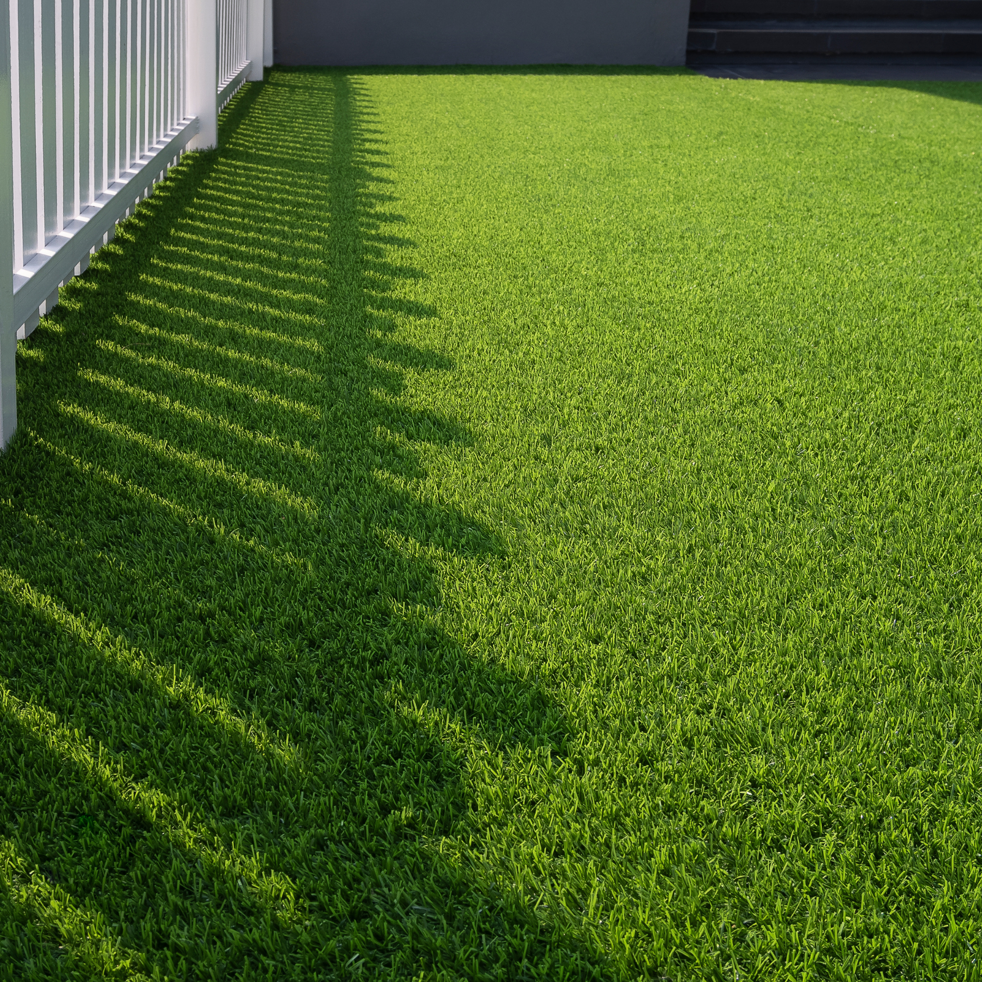 Green Artificial Turf with a white fence and steps in the background