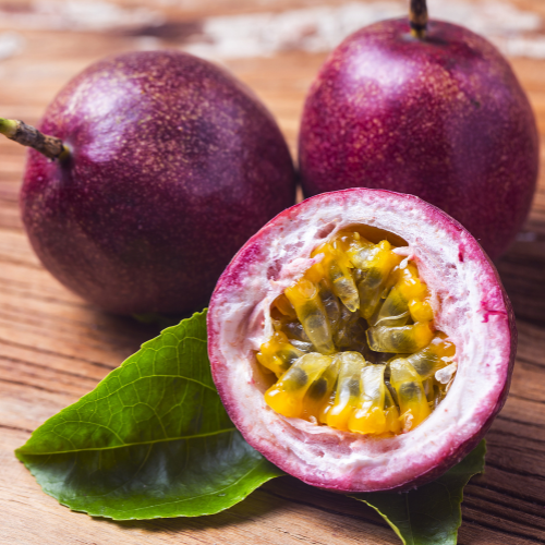 Passion fruit with a cut open one revealing its yellow flesh on a wooden surface.