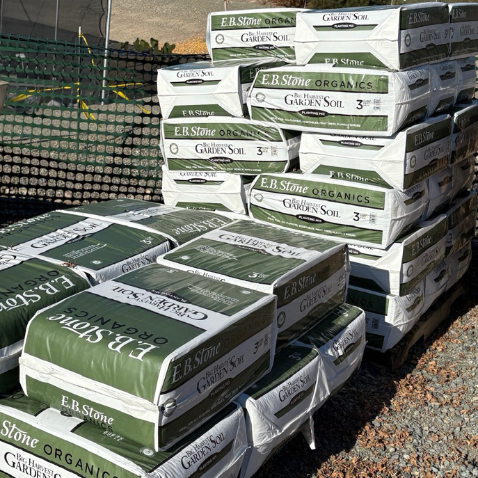 Stack of E.B. Stone Organics bags on a gravel surface with a clear sky.