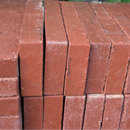 Stack of red bricks with a blurred background of plants and green bags.