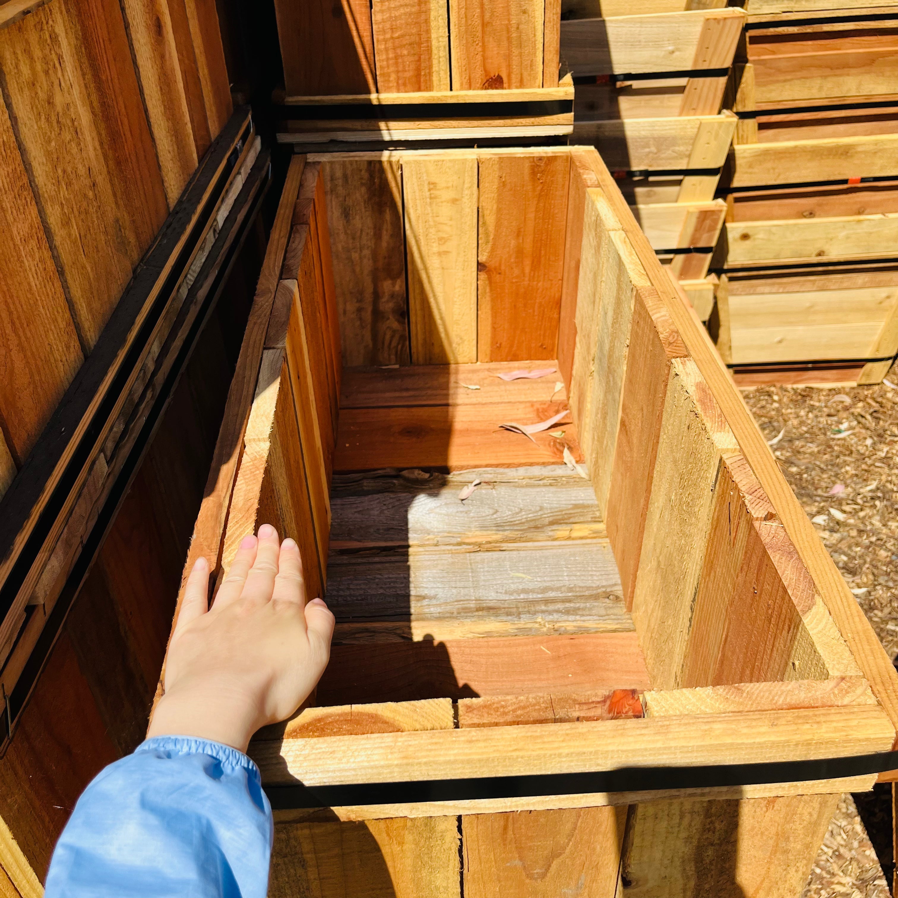 Hand reaching into a wooden crate with more crates stacked in the background
