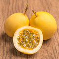 Three Yellow Passion Fruits on a wooden surface, with one cut open to reveal its interior.